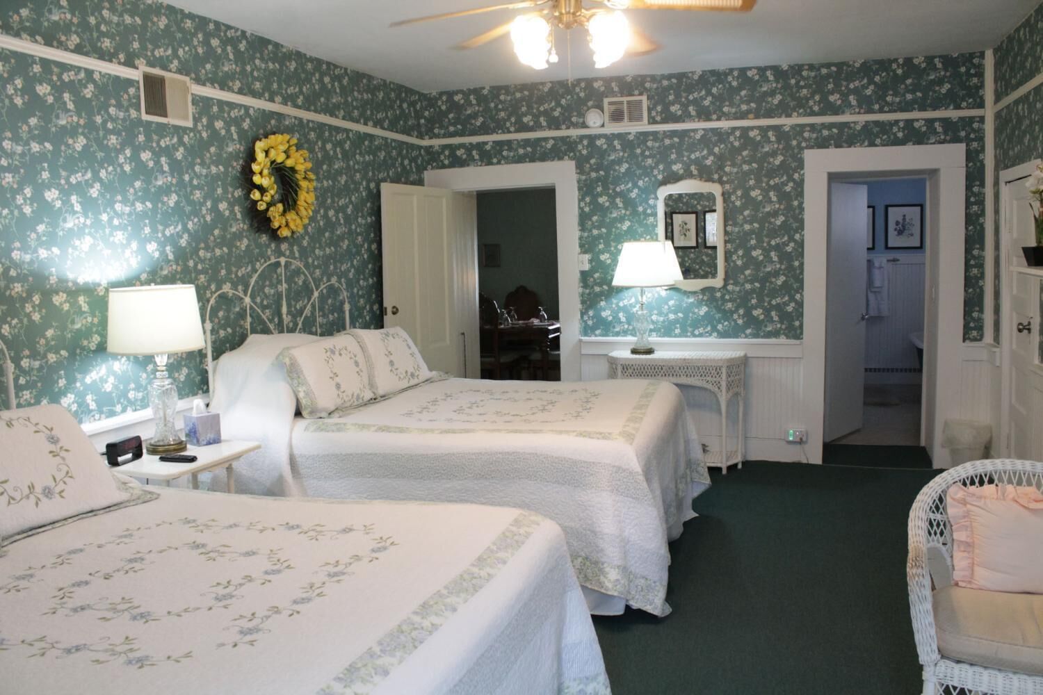A room with two beds, a desk, a chair, a mirror, and a door leading to another room.