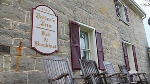 A stone building with a sign for 'Jailer’s Inn Bed & Breakfast'. There are wooden chairs in front of the building.
