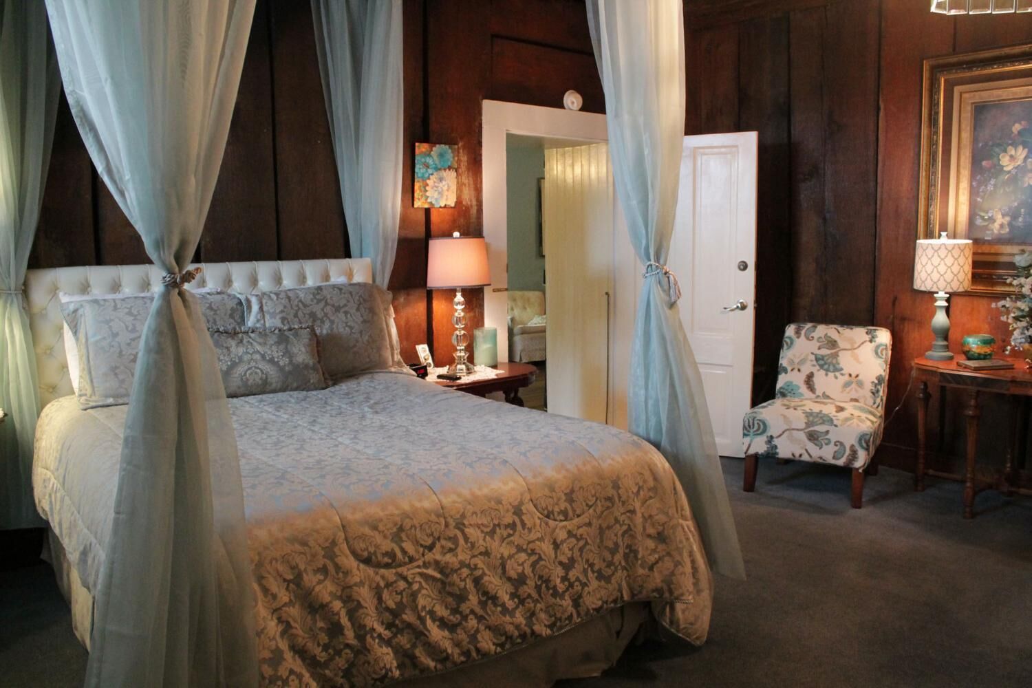 Un dormitorio con cama con dosel, una silla, una lámpara y una puerta.