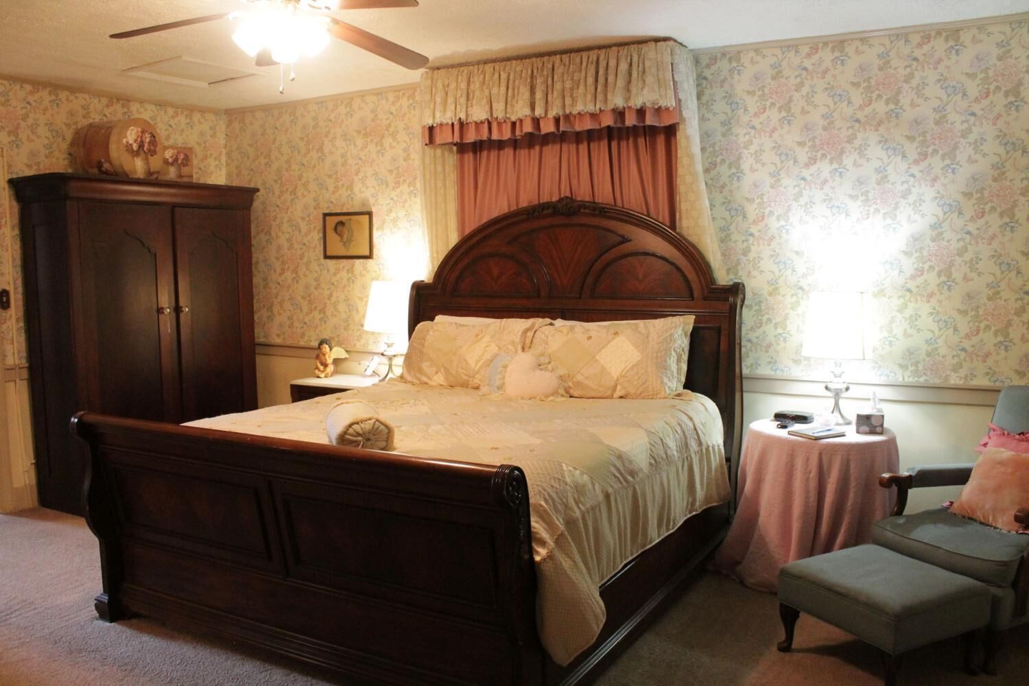 A bedroom with a wooden bed, a nightstand, a chair, and a small table with a lamp.