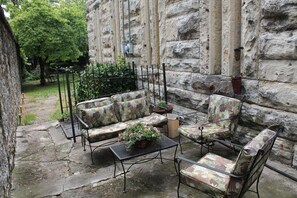 An outdoor seating area with a stone wall backdrop, a metal table, and patterned cushions. - Jailer's Inn (Bardstown)