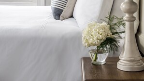 A neatly made bed with white bedding, a striped pillow, and a vase with white flowers on a bedside table.