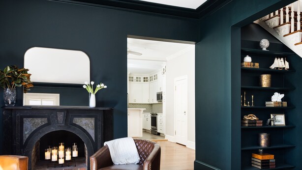 A room with a dark blue wall, a fireplace with lit candles, a leather armchair, and a bookshelf with decorative items.