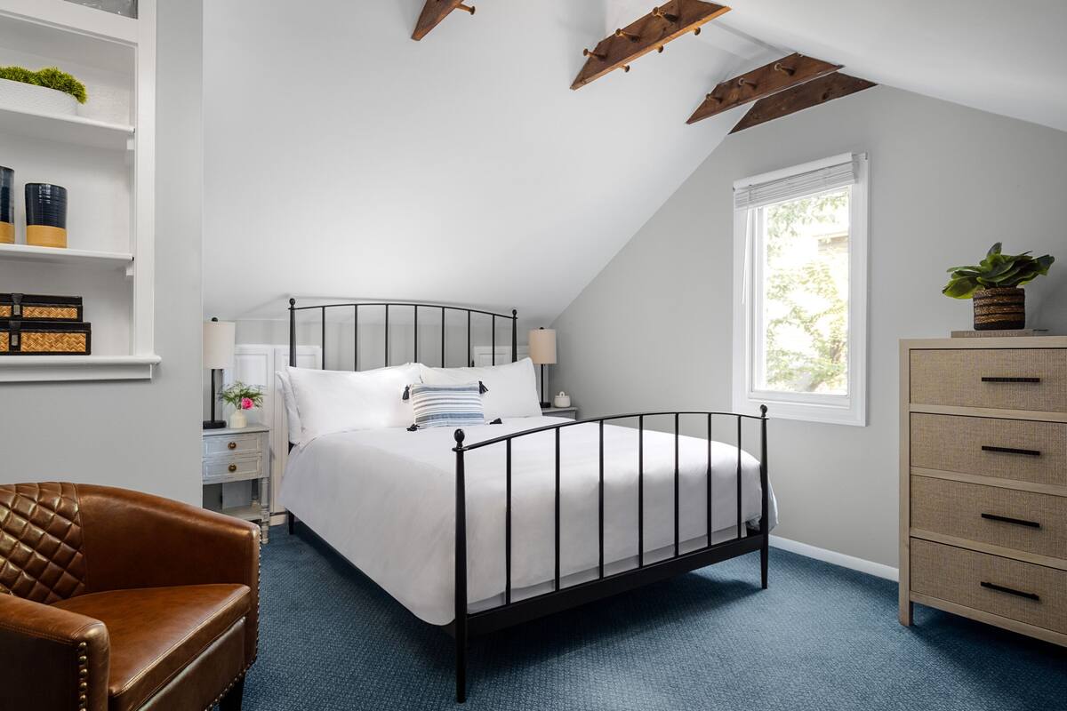 A bedroom with a bed, a chair, a dresser, and a window.