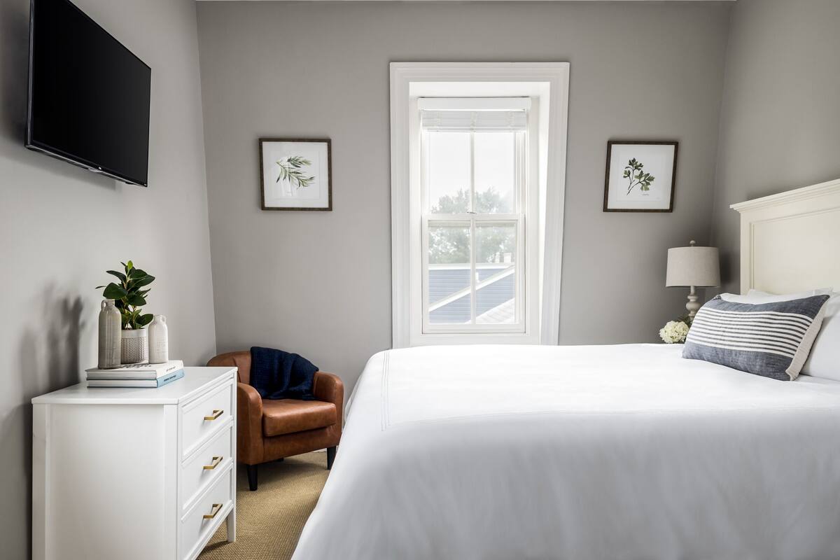 A bedroom with a bed, a dresser, a chair, a TV, and framed pictures on the walls.