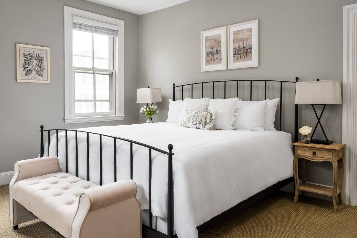 A bedroom with a bed, bedside tables, a bench, and artwork on the walls.