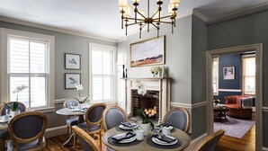 A dining room with a fireplace, wooden chairs, a chandelier, and framed artwork on the walls.