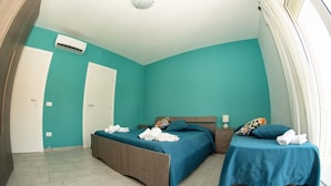 A hotel room with two beds, teal walls, a white door, and a window with curtains. - B&b Villa Kairos (Ioppolo Giancaxio)