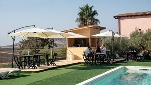 An outdoor pool area with tables and chairs, surrounded by greenery and a view of the countryside. - B&b Villa Kairos (Ioppolo Giancaxio)