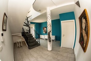 A spacious interior with a curved staircase, a white door, and a teal accent wall. - B&b Villa Kairos (Ioppolo Giancaxio)