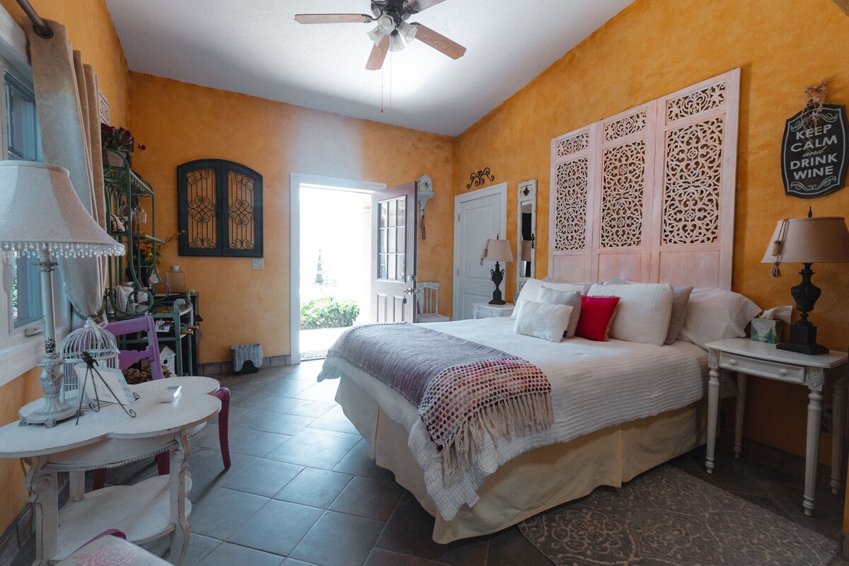 Quarto com cama, mesa de cabeceira, mesa e cadeira. Há uma janela com vista para o exterior.