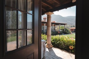 Vista desde una ventana con un pilar de piedra y un jardín con flores, con una montaña al fondo.