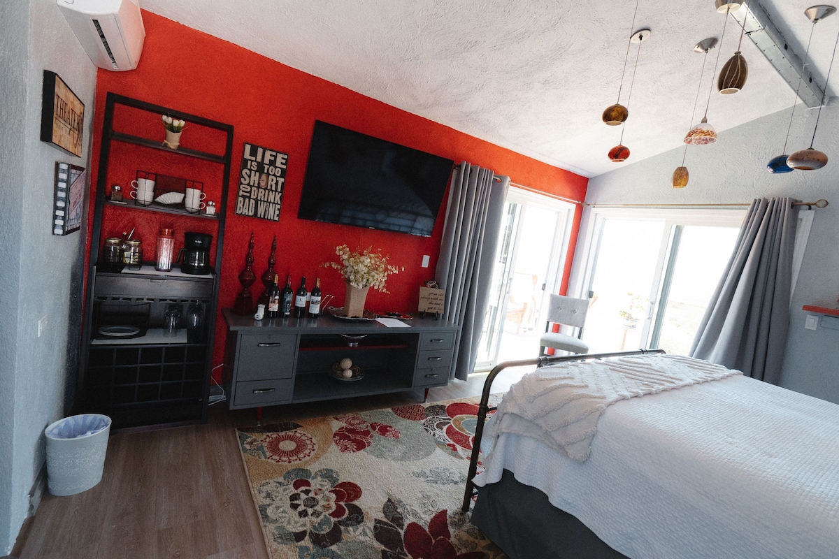 Quarto com cama, televisão na parede, escrivaninha com computador e janela com cortinas.
