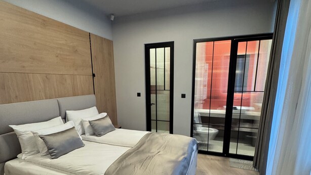 A modern bedroom with a bed, a wooden headboard, a sliding glass door, and a ceiling light. - Urban Flame Apartments (Sarajevo)