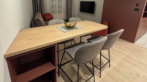 A modern dining area with a wooden table, two bar stools, and pendant lights. - Urban Flame Apartments (Sarajevo)