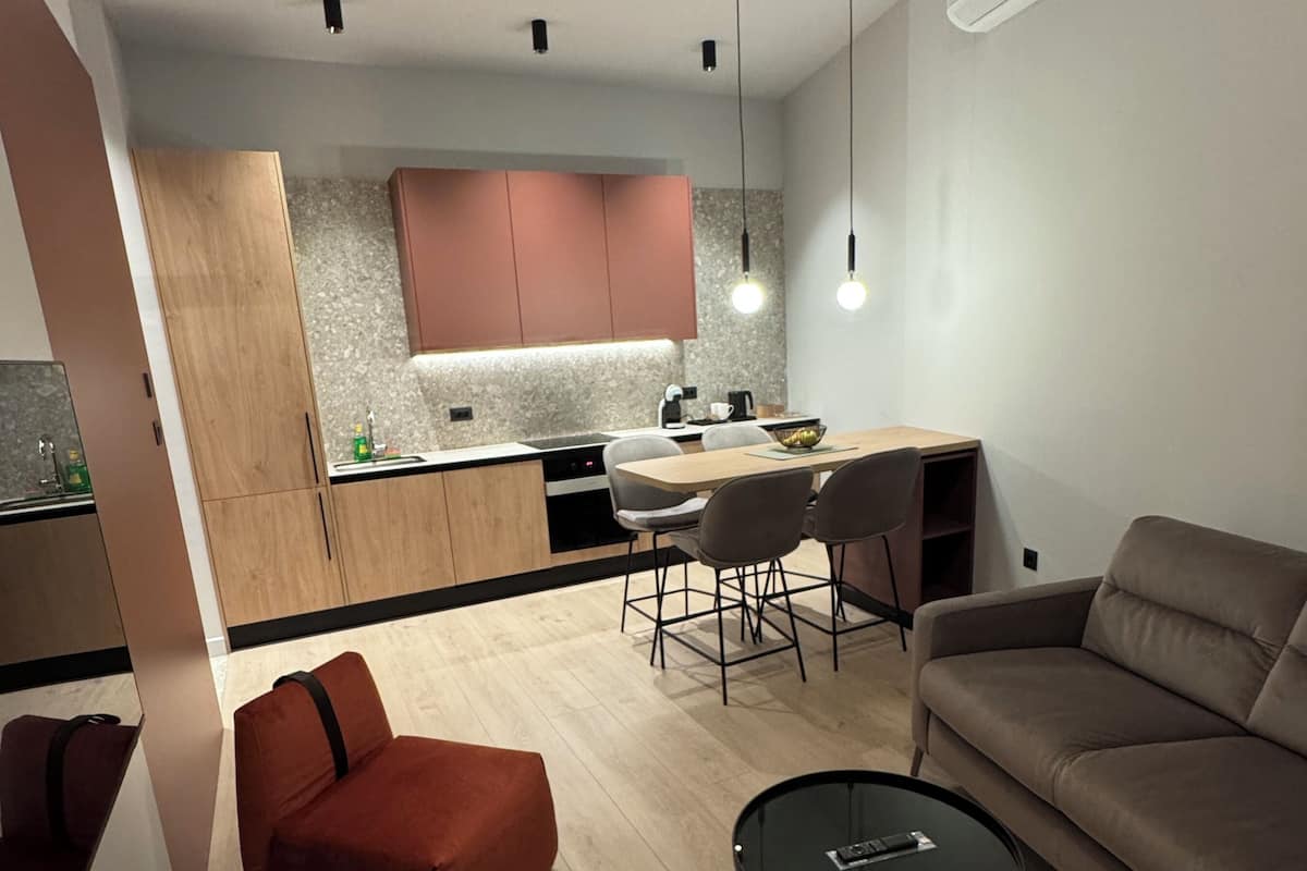 Una sala de estar moderna con un sofá, una silla roja, una mesa de centro de vidrio y un comedor con una mesa y sillas.