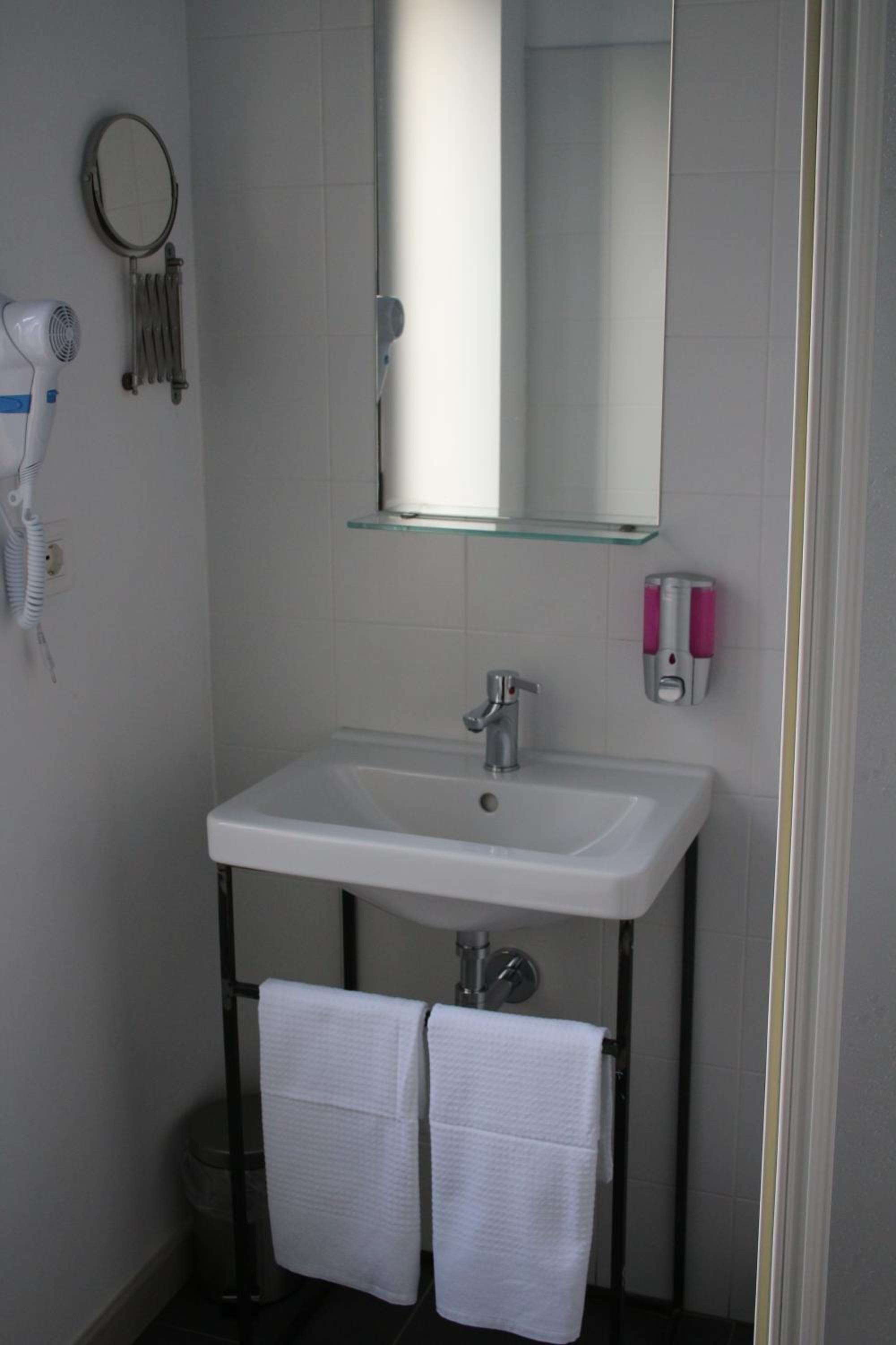 A bathroom with a white sink, a glass shelf above it, a mirror, and two white towels hanging on a rack.