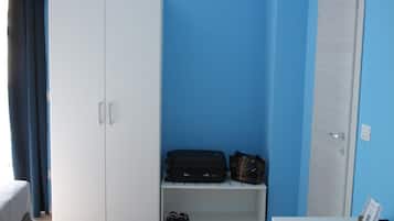 Una habitación con un armario blanco, un banco con una maleta y un bolso, y un par de zapatos en el suelo.