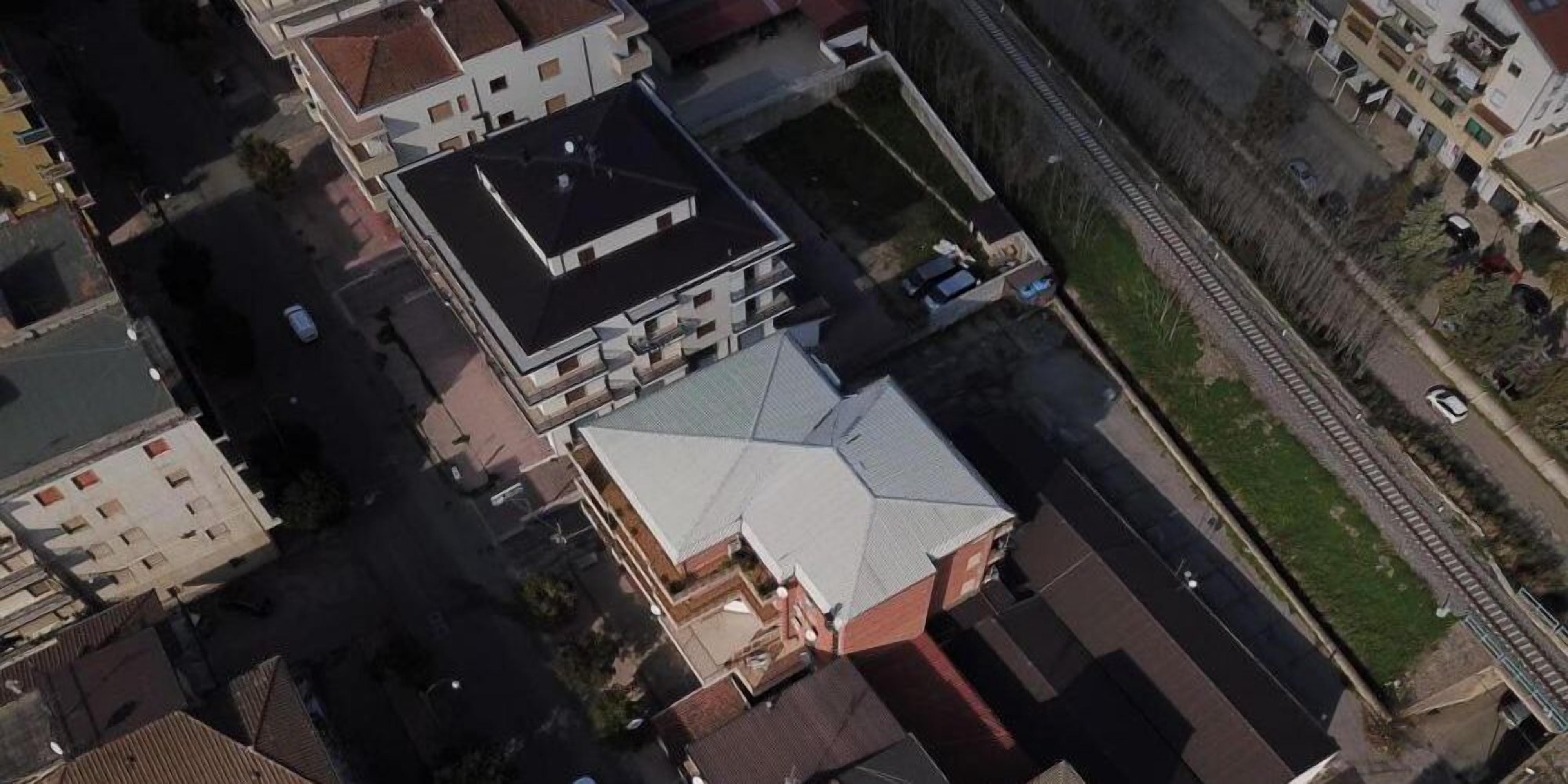An aerial view of a building with a distinct roof structure, adjacent to a railway track.