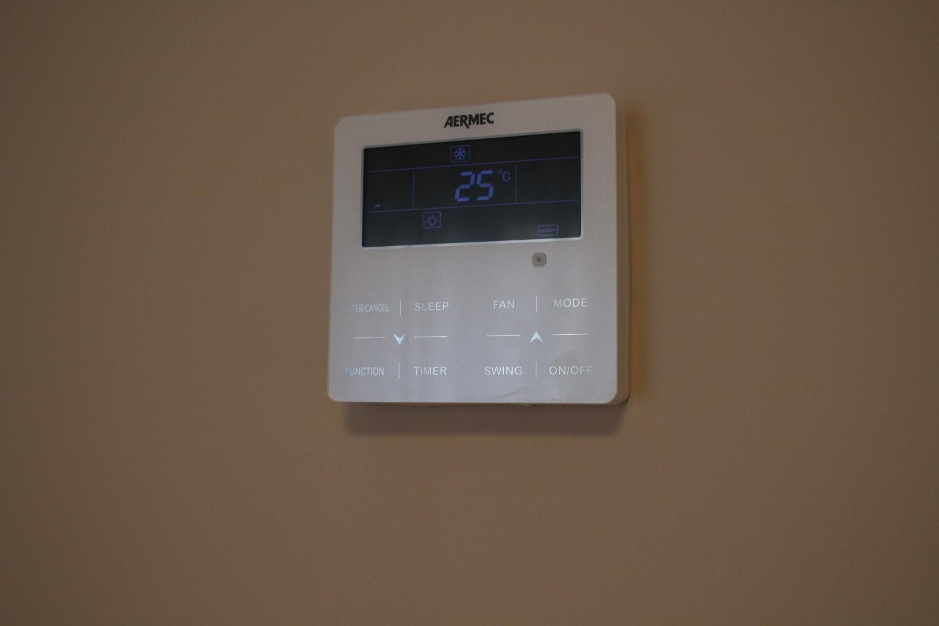 A wall-mounted thermostat with a digital display showing 25°C, featuring buttons for functions, timer, swing, and on/off.