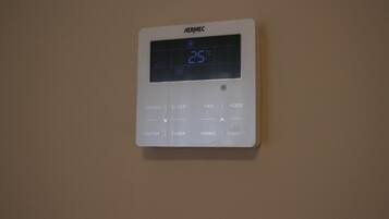A wall-mounted thermostat with a digital display showing 25°C, featuring buttons for functions, timer, swing, and on/off.