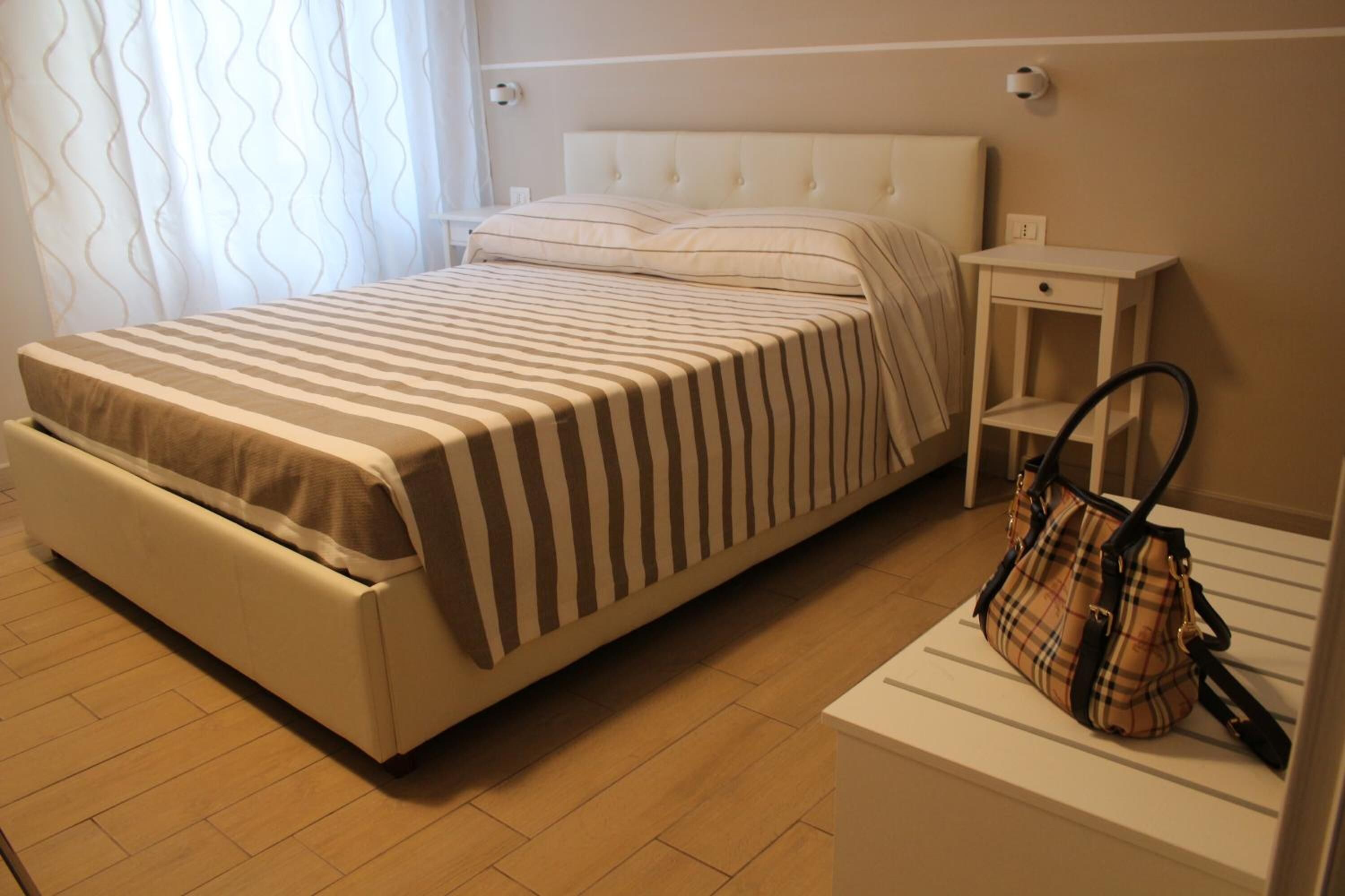 A neatly arranged bedroom with a bed, bedside table, and a handbag on a shelf.