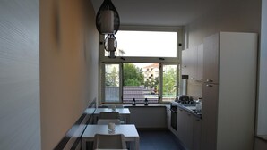 A compact kitchen with a dining area, a window with a view of buildings, and a modern pendant light.