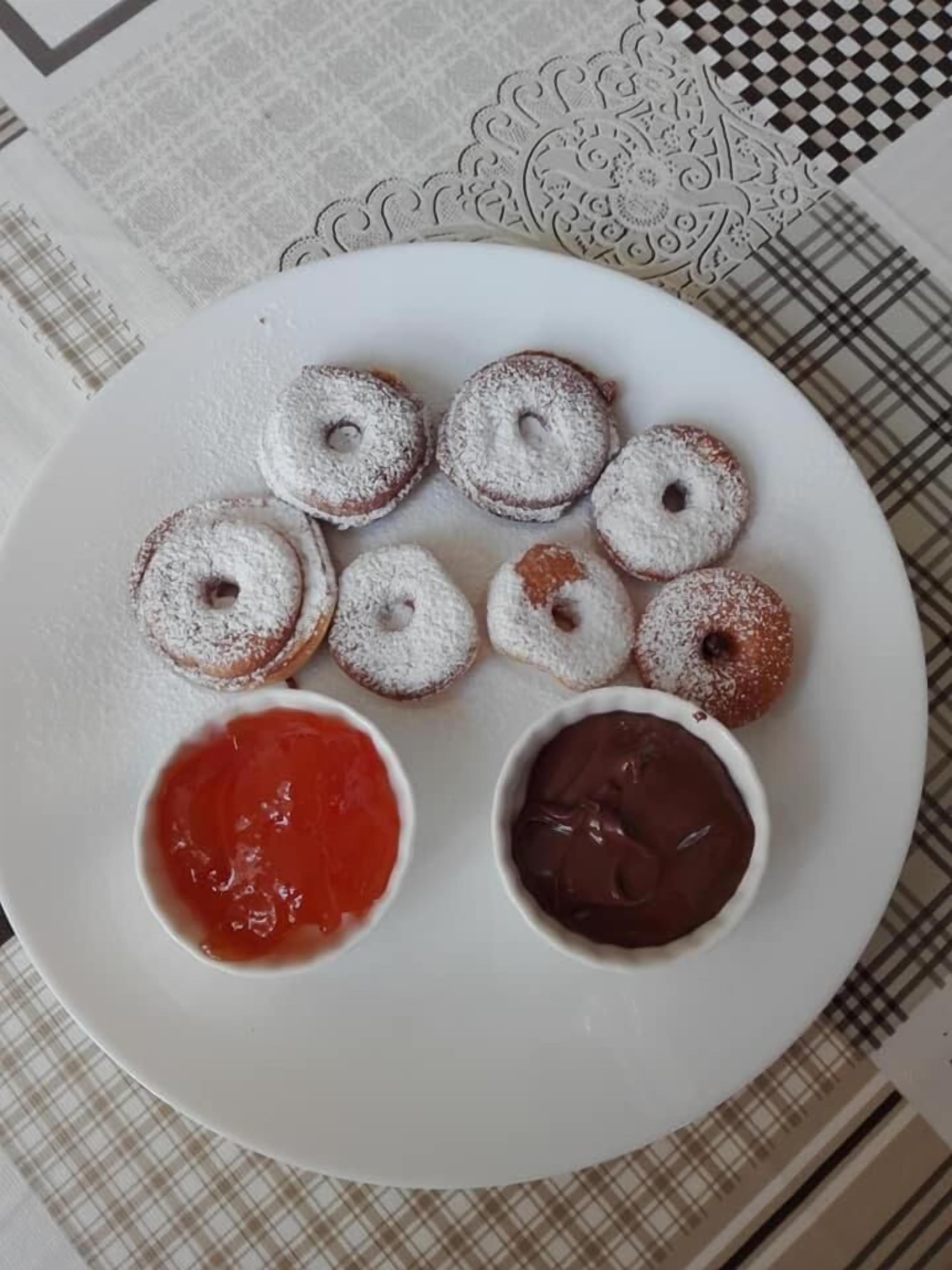 Ein Teller mit sechs mit Puderzucker bestäubten Donuts und zwei kleinen Schalen rote und Schokoladensauce.