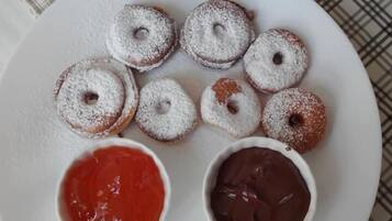 Ein Teller mit sechs mit Puderzucker bestäubten Donuts und zwei kleinen Schalen rote und Schokoladensauce.