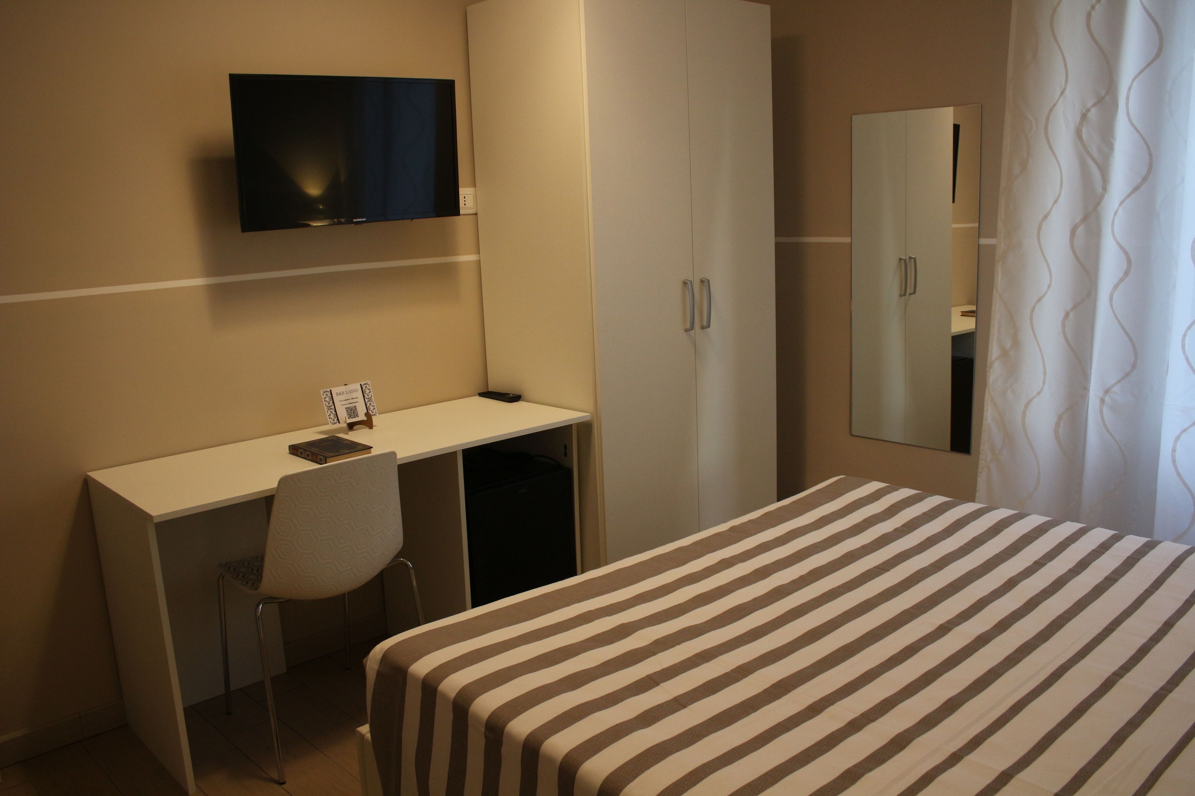 Habitación de hotel con cama, escritorio, silla, televisión, armario y espejo.