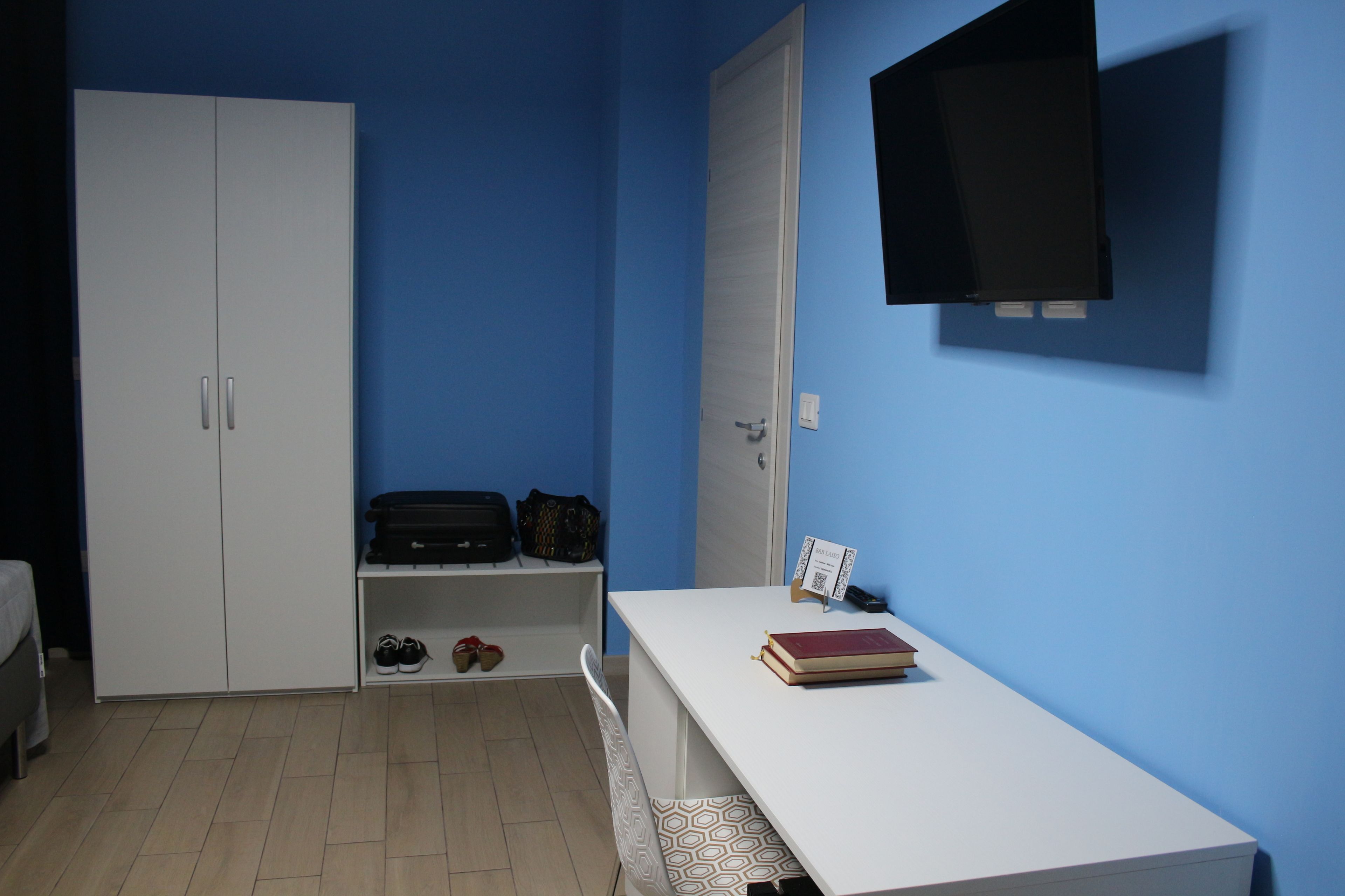Une pièce avec un bureau blanc, une bibliothèque, une armoire et un téléviseur fixé au mur.