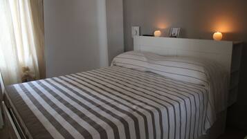 Uma cama bem arrumada com roupa de cama listrada, um painel de cabeceira branco e duas luminárias laterais.
