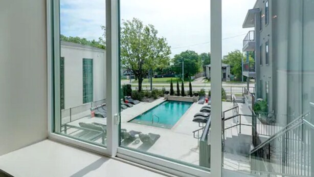 Un edificio moderno con amplios ventanales que dan a una piscina y zonas ajardinadas.