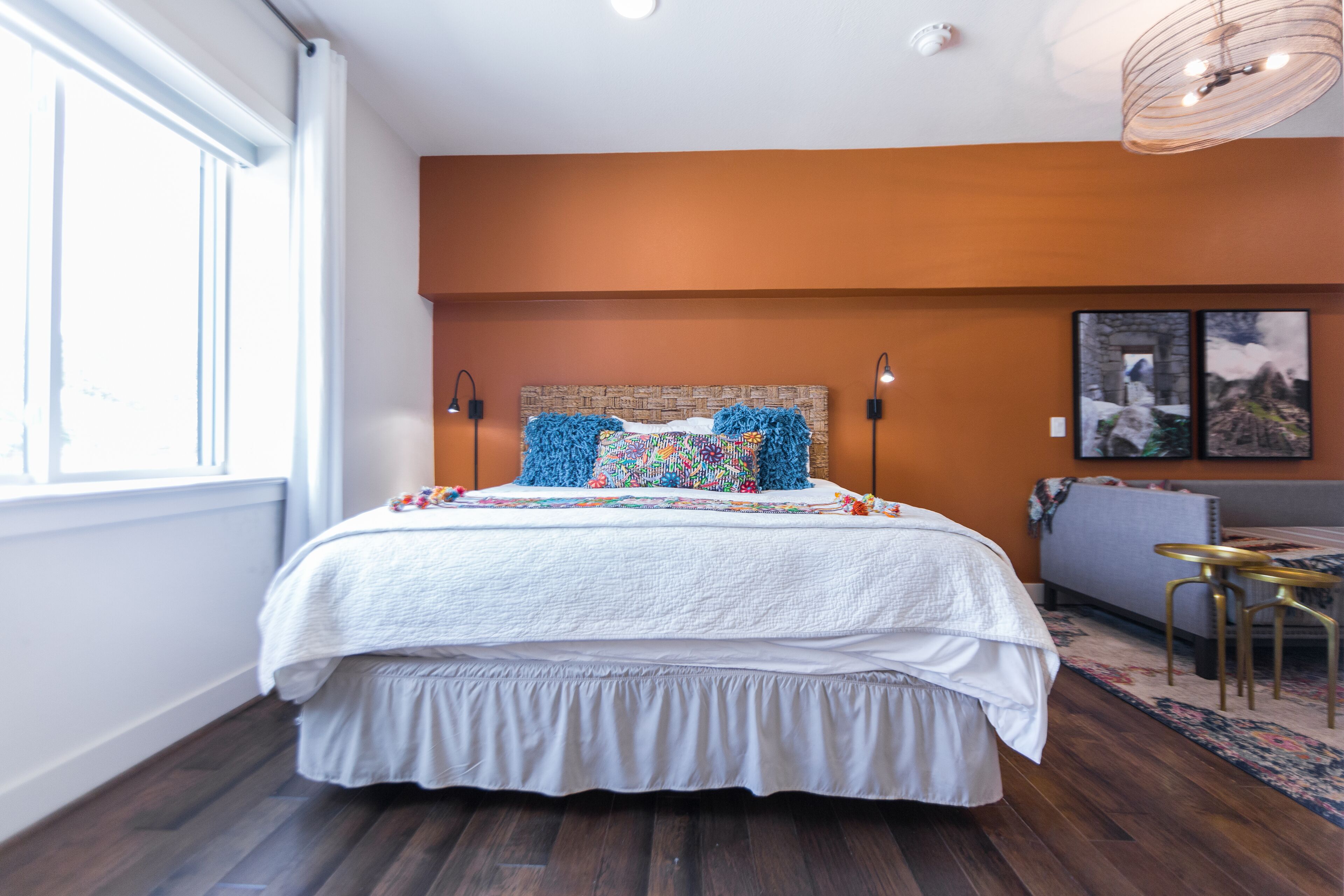 Un dormitorio con una cama grande, una ventana, una obra de arte colgada en la pared y una pequeña mesa con dos sillas.