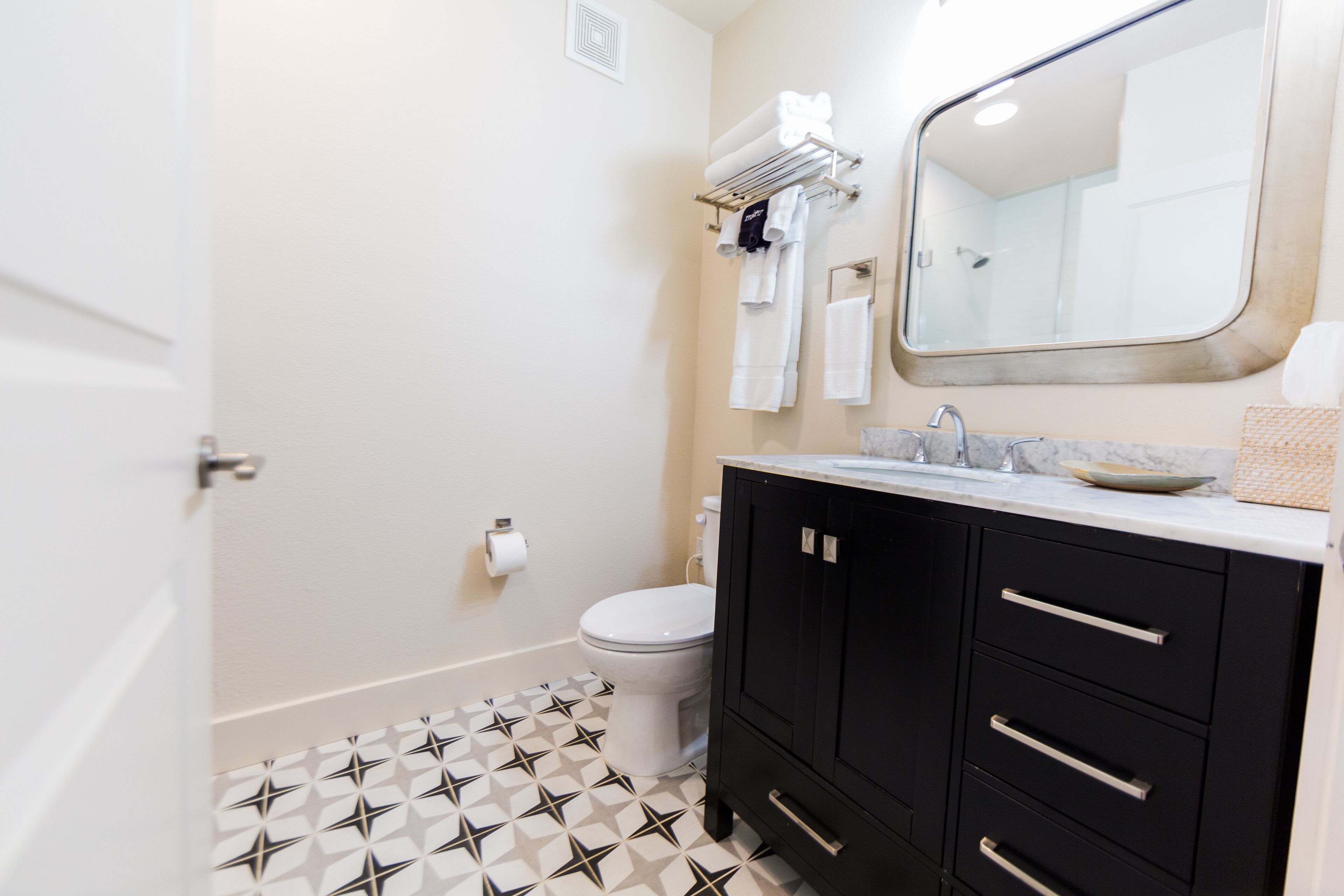 A bathroom with a toilet, sink, and mirror. There is a towel rack with towels and a toilet paper roll on the wall.