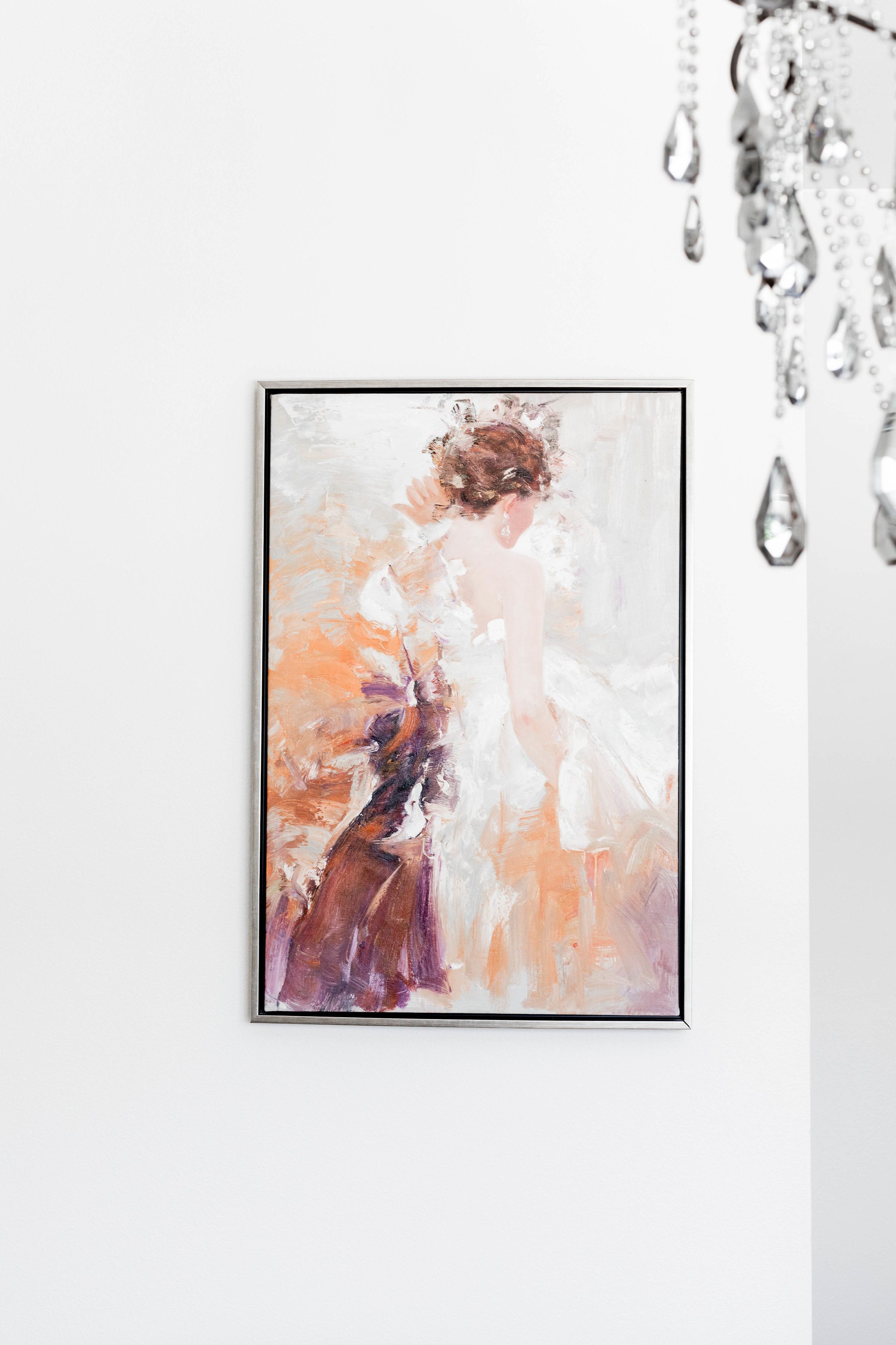 Une peinture abstraite encadrée représentant une femme en robe, accrochée à un mur blanc.