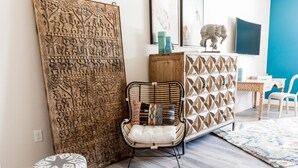 Una habitación con un gran panel de madera tallada, una silla de mimbre con cojines, un reposapiés estampado, un mueble con motivos geométricos y una pared azul.