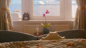 A bedroom with a large window, a bed, a chandelier, and a view of the sea. - Tigh Na Mara (Fortrose)