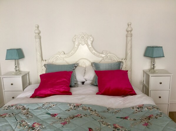 A bed with a floral quilt, white headboard, and two nightstands with lamps.