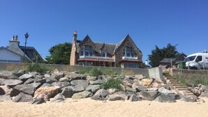 A large, historic house with multiple balconies and a stone facade, situated on a sandy beach with a rocky foreground. - Tigh Na Mara (Fortrose)