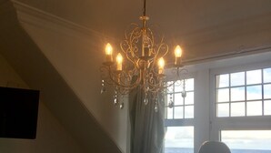 A room with a chandelier, a view of the sea through a window, a blue armchair, and a white decorative object. - Tigh Na Mara (Fortrose)