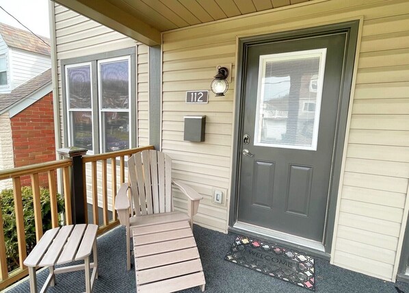 A front porch with a wooden chair and a welcome mat. - Escape to our cozy retreat, just a 10-min drive to Greensburg (Youngwood)