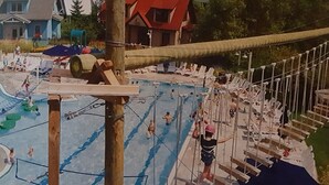 Ein Schwimmbecken mit einer Seilbrücke, Liegestühlen und einem Gebäude im Hintergrund.