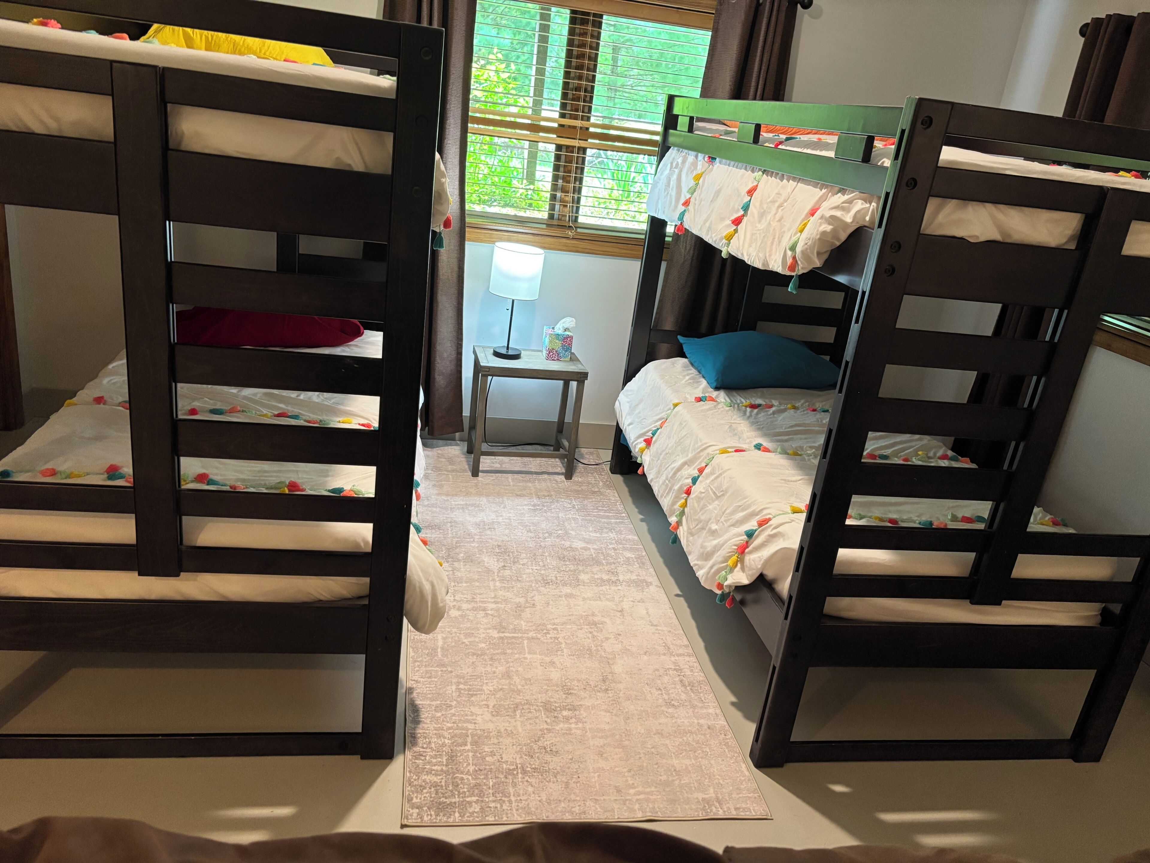 A bunk bed room with a small table and a window with blinds.