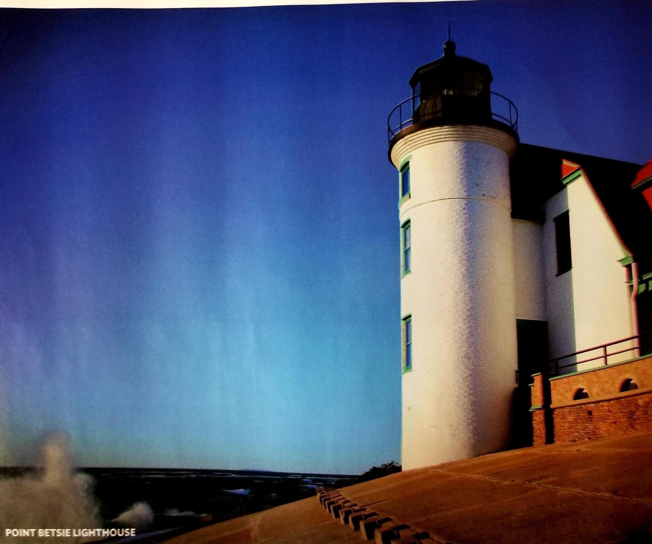 Um farol com exterior branco e topo preto, localizado ao lado de um edifício com fachada vermelha e verde.