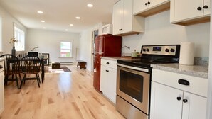 A modern kitchen with white cabinets, stainless steel appliances, and a wooden dining area.