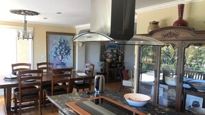 Una cocina moderna con una isla central, sillas de madera, una mesa de comedor y un amplio ventanal con vistas a un jardín.