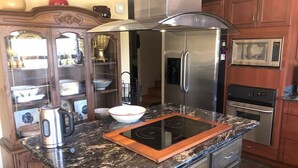 Una cocina con refrigerador de acero inoxidable, microondas, horno, estufa integrada y un armario de madera con puertas de vidrio.