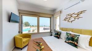 A hotel room with a bed, a yellow armchair, a view of the pool, and a wall-mounted TV. - LIBERTY &  FREEDOM villa, helipad and pools!Perfect for large groups up to 16 ! (Platanias)
