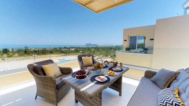 A balcony with wicker furniture, a dining table set with plates, cups, and a fruit bowl. - LIBERTY &  FREEDOM villa, helipad and pools!Perfect for large groups up to 16 ! (Platanias)